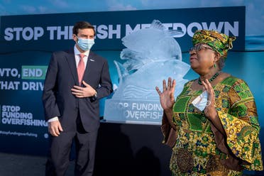 WTO Director-General Ngozi Okonjo-Iweala gestures next to WTO Colombian Ambassador Santiago Wills with an ice sculpture depicting fish in the background during an event by NGOs requesting urgent action to finalize the WTO agreement on ending subsidies that drive overfishing, in Geneva, Switzerland, on March 1, 2021. (Reuters)