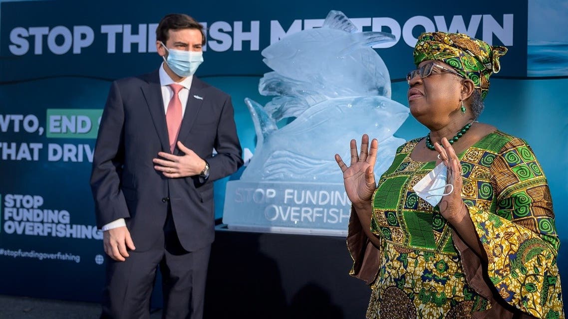 WTO Director-General Ngozi Okonjo-Iweala gestures next to WTO Colombian Ambassador Santiago Wills with an ice sculpture depicting fish in the background during an event by NGOs requesting urgent action to finalize the WTO agreement on ending subsidies that drive overfishing, in Geneva, Switzerland, on March 1, 2021. (Reuters)