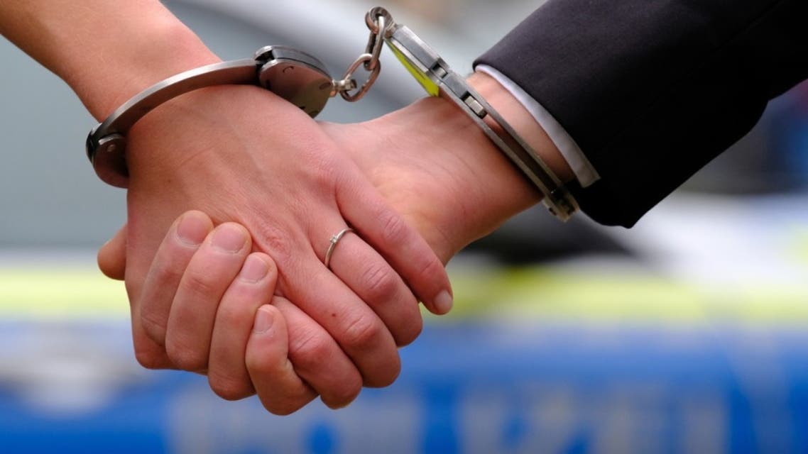 Young couple with hand-cuffs in front of a police car stock photo