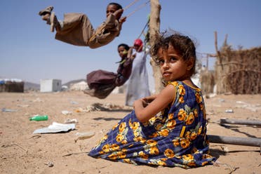 A girl sits as other children play on swings at a camp for internally displaced people in Marib, Yemen Feb. 16, 2021. (Reuters)