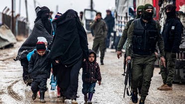 A veiled woman walks with children next to a member of the Syrian Kurdish internal security services known as Asayish at al-Hol camp in Hasakeh governorate in northeastern Syria, on January 19, 2021.  (Delil Souleiman/AFP)