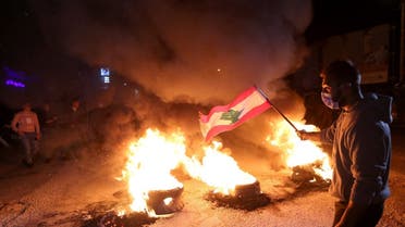 A demonstrator holds a Lebanese flag as he stands near burning tires during a protest against the fall in Lebanese pound currency and mounting economic hardship, March 2, 2021. (Reuters)