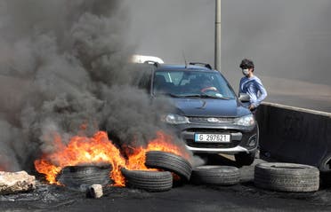 A woman tries to cross a blocked road with burning tires during a protest against the fall in Lebanese pound currency and mounting economic hardships in Khaldeh, Lebanon March 8, 2021. (Reuters)