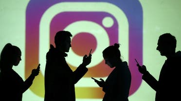 Silhouettes of mobile users are seen next to a screen projection of Instagram logo in this picture illustration. (Reuters)
