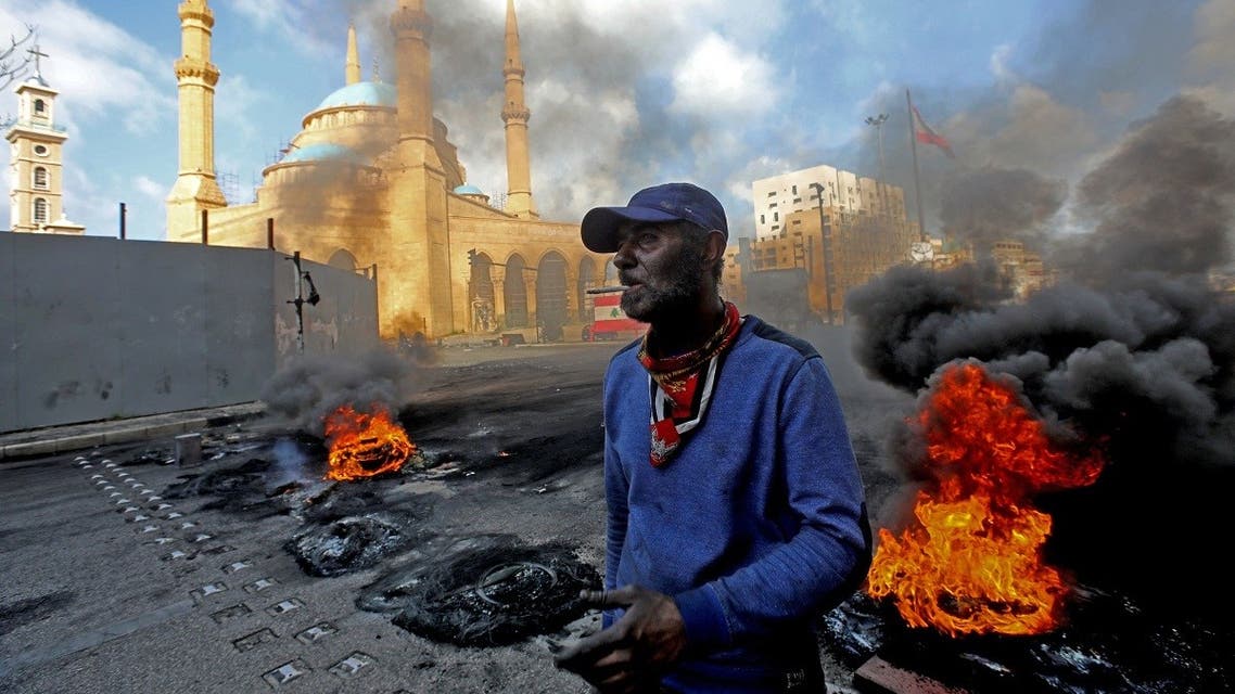 A man stands next to flaming tires at a make-shift roadblock set-up by anti-government demonstrators next to the Mohammed al-Amin Mosque in the Martyrs' Square in the center of Beirut on March 8, 2021. (Anwar Amro/AFP)
