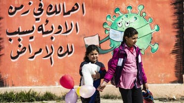 Syrian children cross a road in front of a mural awareness campaign drawing calling on people to take care as the COVID-19 pandemic spreads all over the world in Syria's northeastern city of Qamishli on March 9, 2021. (AFP)
