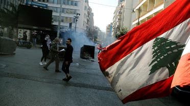 An anti-government demonstrator waves the national flag as they block the street, with burning garbage dumpsters, in front of Lebanon's central bank in the capital Beirut on March 16, 2021. (Joseph Eid/AFP)