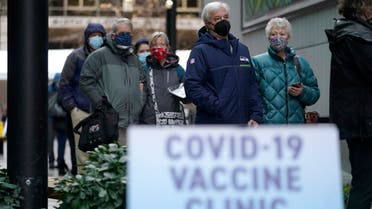 People stand near a sign as they wait in line to receive the first of two doses of the Pfizer vaccine for COVID-19, at a one-day vaccination clinic set up in an Amazon.com facility in Seattle and operated by Virginia Mason Franciscan Health.  (AP)