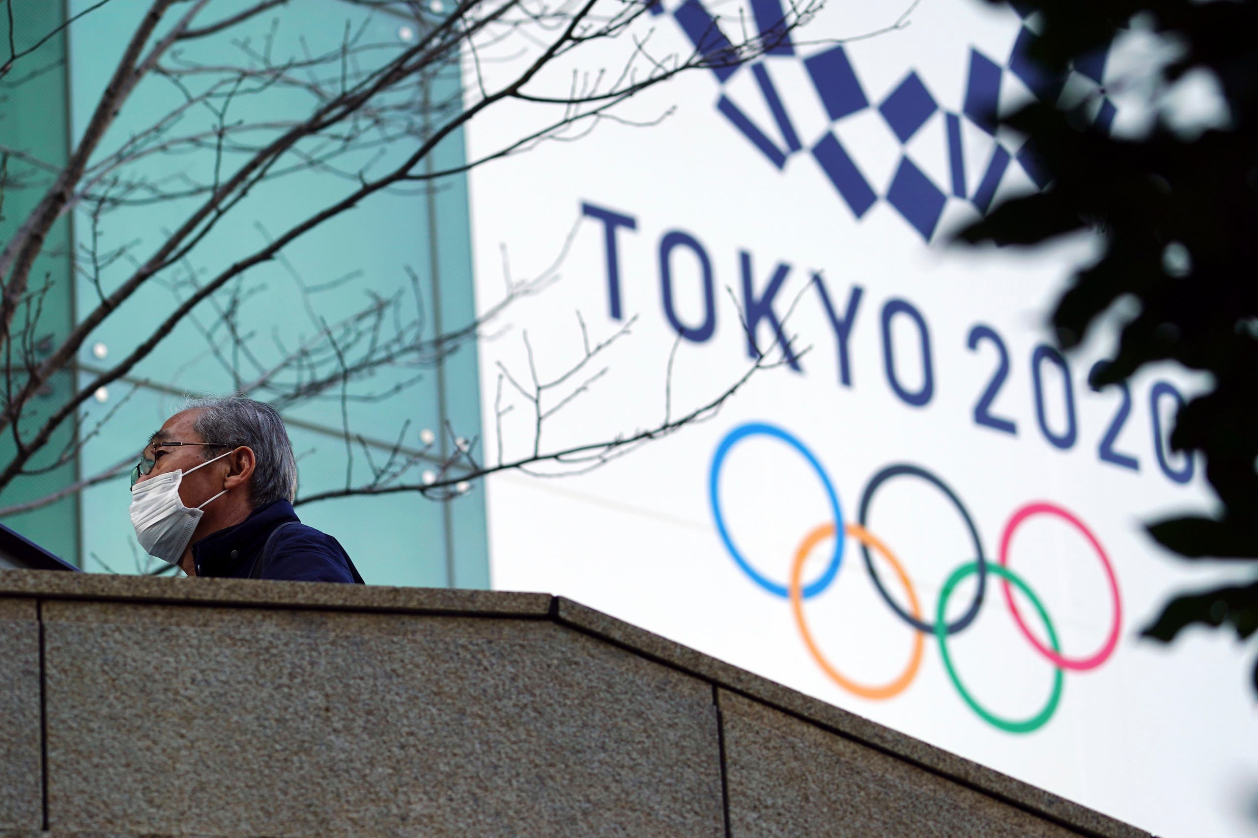 A man wearing a protective mask to help curb the spread of the coronavirus walks near the banner for the Tokyo 2020 Olympic Games Thursday, Feb. 25, 2021. (File photo: AP)