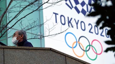 A man wearing a protective mask to help curb the spread of the coronavirus walks near the banner for the Tokyo 2020 Olympic Games Thursday, Feb. 25, 2021. (File photo: AP)