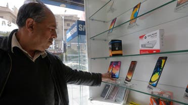 A man checks mobile phones displayed in a shop in the Syrian capital Damascus, on March 24, 2021. (Louai Beshara/AFP)