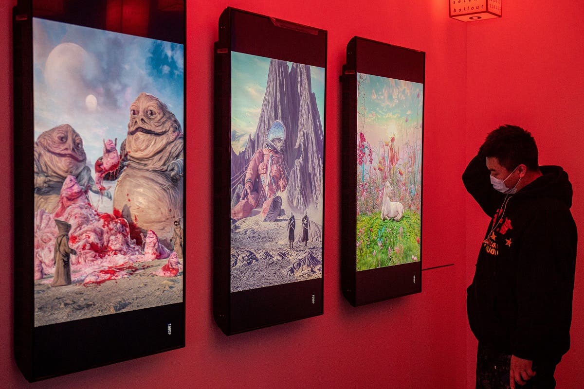 A man looks at digital paintings by US artist Beeple at a crypto art exhibition entitled “Virtual Niche: Have You Ever Seen Memes in the Mirror,” one of the world’s first physical museum shows of blockchain art, ahead of its opening in Beijing on March 26, 2021. (Reuters)