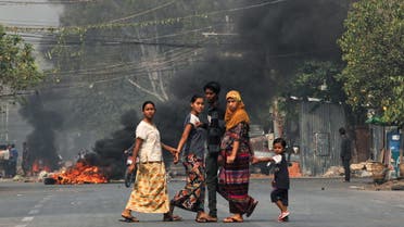 People walk on a street as barricades burn behind them during a protest against the military coup, in Mandalay, Myanmar March 27, 2021. (Reuters)