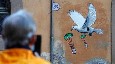 A man takes a picture of a mural depicting a white dove parachuting COVID-19 vaccine vials, posted near the Italian Health Ministry Headquarters in Rome, Sunday, April 4, 2021. (AP/Gregorio Borgia)