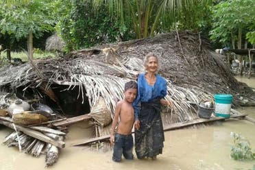 An elderly villager and her grandson stand in floodwaters in front of their damaged home in the village of Haitimuk in East Flores on April 4, 2021, after flash floods and landslides swept eastern Indonesia and neighbouring East Timor. (File photo: AFP)