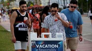 A group of men read public safety precautions while enjoying the bars and restaurants on South Beach during Spring Break amid the COVID-19 pandemic, March 27, 2021. (Reuters) 