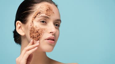 Beautiful woman applying coffee scrub on face, isolated on blue stock photo