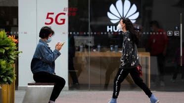 A woman wearing a face mask to help curb the spread of the coronavirus browses her smartphone as a masked woman walks by the Huawei retail shop promoting it 5G network in Beijing. (File photo: AP)