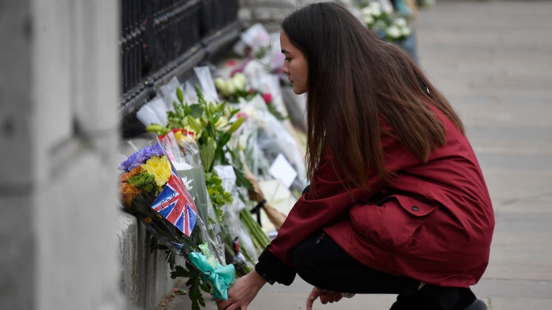 A woman places flowers at the gate of Buckingham Palace in London, one day after the death of Britain's Prince Philip, Saturday, April 10, 2021. Britain's Prince Philip, the irascible and tough-minded husband of Queen Elizabeth II who spent more than seven decades supporting his wife in a role that mostly defined his life, died on Friday. (AP Photo/Alberto Pezzali)