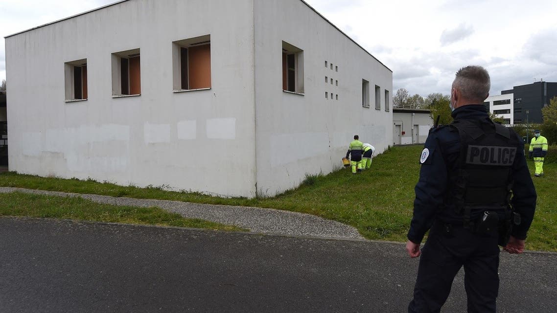 A French police officer watches municipal workers painting the exterior walls of the Avicenna Islamic Cultural center in an attempt to cover-up anti-Muslim graffiti discovered by early morning Muslim worshippers in Rennes, western France on April 11, 2021. (Jean-Francois Monier/AFP)