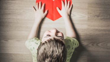 A child holding a heart cut out of paper. (Unsplash)
