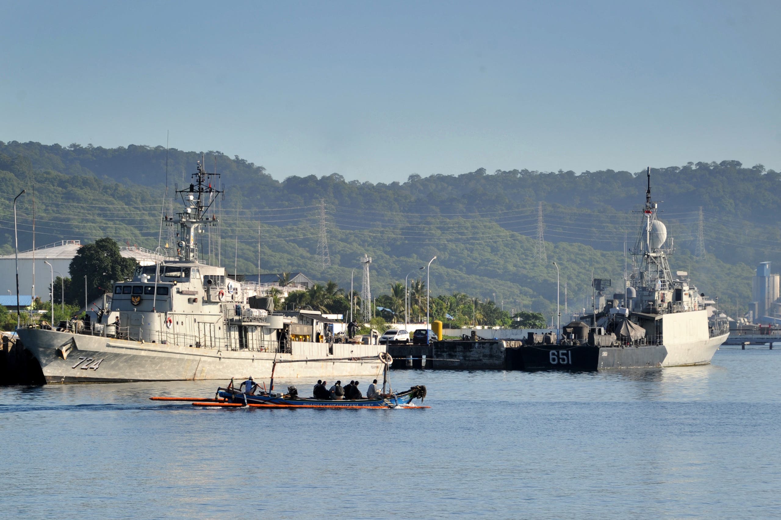 An outrigger canoe sails past Indonesian Navy ships at the naval base in Banyuwangi, East Java province, on April 24, 2021, as the military continues search operations off the coast of Bali for the Navy's KRI Nanggala submarine that went missing April 21 during a training exercise. (AFP)