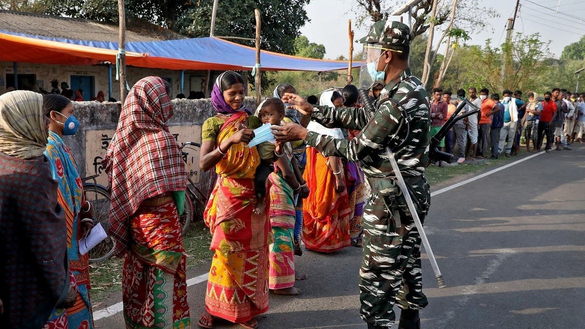 A policeman gives a face mask to a woman as she and others wait in line to cast their vote outside a polling station during the first phase of West Bengal state election in Purulia district, India, on March 27, 2021. (Reuters)