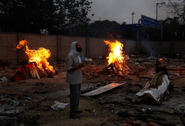 A man stands next to a funeral pyre of a relative who died from the coronavirus disease, during a mass cremation, at a crematorium in New Delhi, India May 1, 2021. (Reuters/Adnan Abidi)