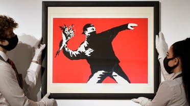 Gallery technicians display a Banksy called Love is in the Air screenprint in colours, 2003, on wove paper, numbered 412/500 in pencil at Christie's auction rooms in London, on March 26, 2021.  (AP)