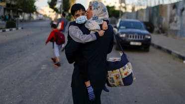 A Palestinian woman carrying her son evacuates after their tower building was hit by Israeli air strikes, amid a flare-up of Israeli-Palestinian violence, in Gaza City May 12, 2021. (Reuters)
