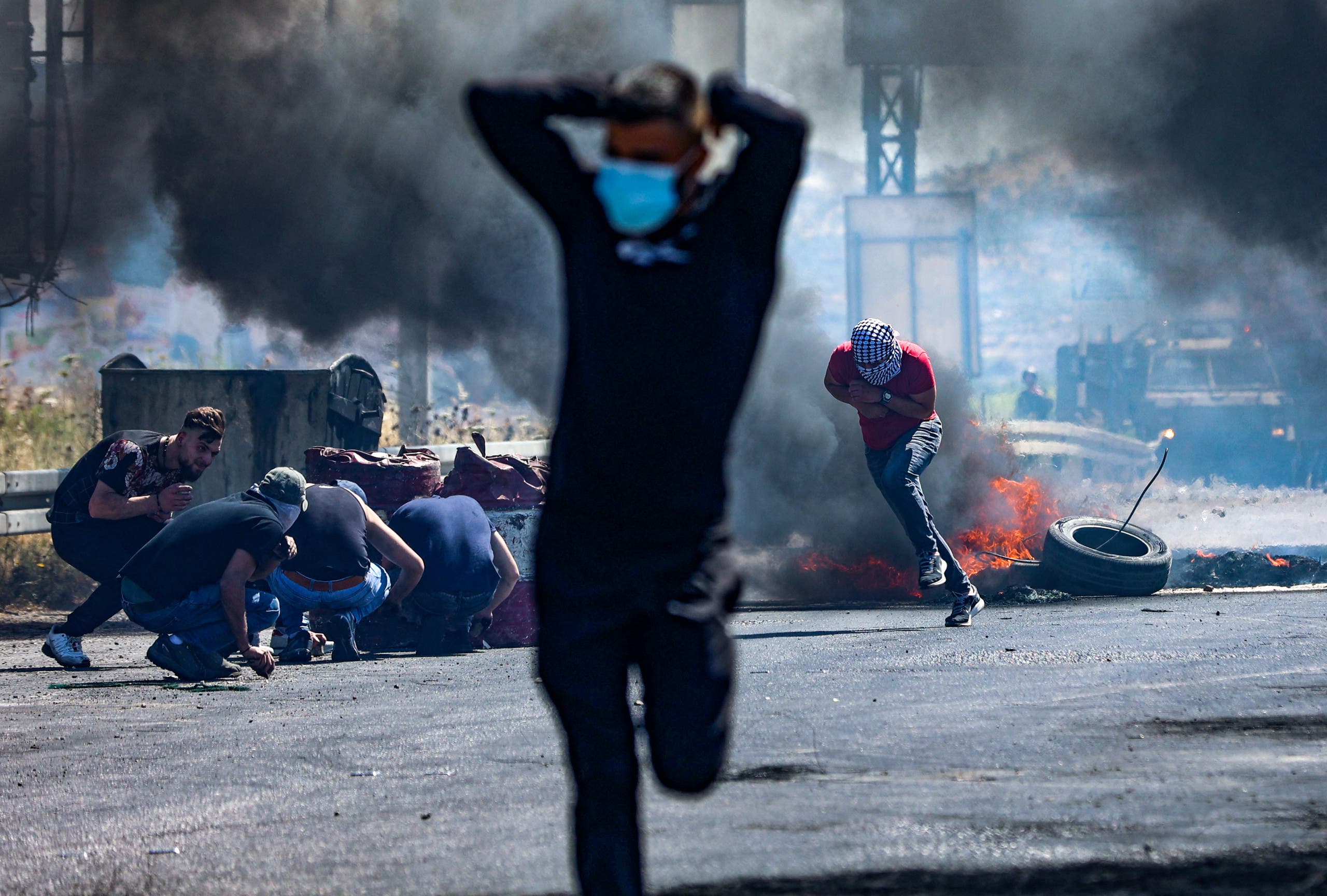 Palestinians run as others take cover, during confrontations with Israeli security forces near the Hawara checkpoint south of the occupied West Bank city of Nablus, on May 14, 2021. (AFP)