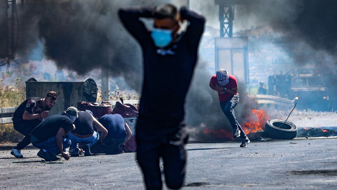 Palestinians run as others take cover, during confrontations with Israeli security forces near the Hawara checkpoint south of the occupied West Bank city of Nablus, on May 14, 2021. (AFP)