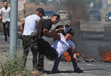 Palestinians carry an injured man to safety, after Israeli security forces launch attacks near the Hawara checkpoint south of the occupied West Bank city of Nablus, on May 14, 2021. (AFP)