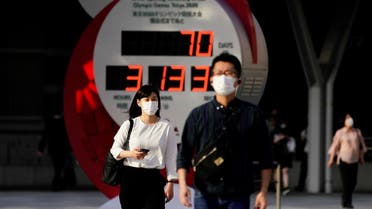 Passersby wearing protective face masks walk near a countdown clock of Tokyo 2020 Olympic Games that have been postponed to 2021 due to the coronavirus outbreak, in Tokyo, Japan, on May 14, 2021. (Reuters)