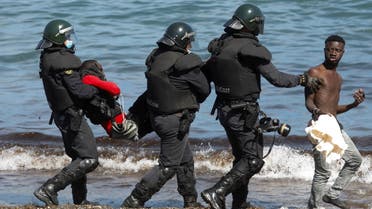 Spanish security forces members carry and escort Moroccan citizens at El Tarajal beach, near the fence between the Spanish-Moroccan border, after thousands of migrants swam across this border during last days, in Ceuta, Spain, May 18, 2021. (Reuters)