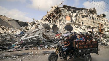 A Palestinian man transports children in a tricycle past the Al-Shuruq building, destroyed by an Israeli air strike, in Gaza City on May 21, 2021, after a ceasefire has been agreed between Israel and Hamas. A ceasefire between Israel and Hamas, the Islamist movement which controls the Gaza Strip, appeared to hold today after 11 days of deadly fighting that pounded the Palestinian enclave and forced countless Israelis to seek shelter from rockets.