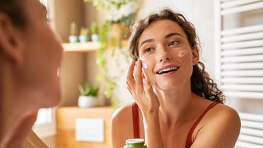 Woman applying moisturiser on face during morning routine stock photo