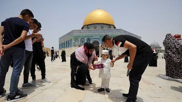 A Palestinian woman offers sweets to a boy before Friday prayer near Al-Aqsa Mosque, May 21, 2021. (Reuters)