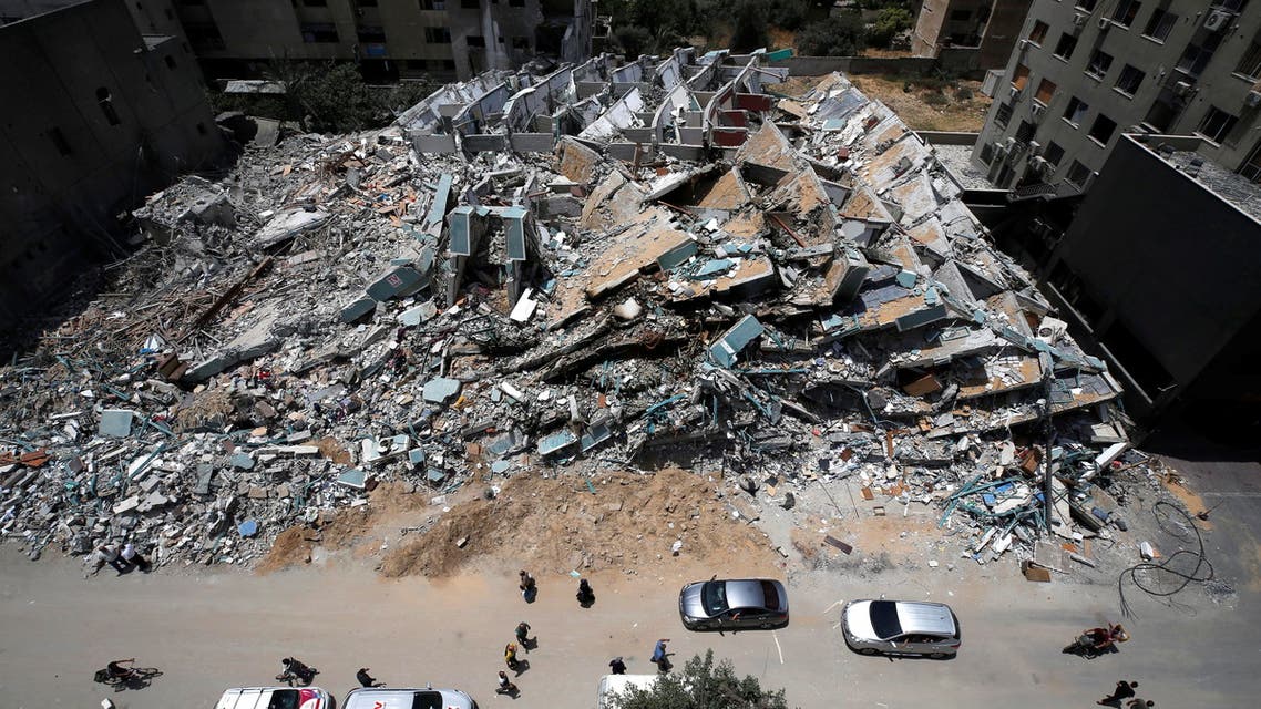 Palestinians walk as cars drive past the remains of a tower building destroyed by Israeli missile strikes in the recent cross-border violence. (Reuters)