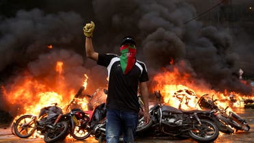 A demonstrator gestures as motorcycles that are are impounded for violating traffic regulations are seen on fire at the municipal yards, in Popayan, Colombia May 28, 2021. (Reuters)