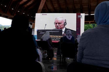 Women from Srebrenica watch a live broadcast from the Yugoslav War Crimes Tribunal in The Hague to learn the verdict for Bosnian Serb military chief Ratko Mladic, on the screen, at the memorial cemetery in Potocari near Srebrenica, eastern Bosnia, Tuesday, June 8, 2021. (AP/Darko Bandic)