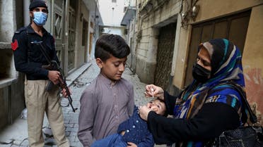 A Police officer stands guard while a health worker administers a polio vaccine to a child, in Peshawar, Pakistan, on March 29, 2021. (AP)