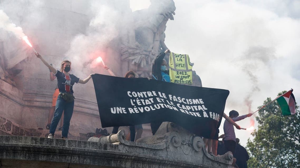 Protestors stand with smoke flares and a banner reading 'Against fascism, the state and capitalism, a new revolution needs to be done' on the statue at Place de la Republique as they take part in a Freedom march called by several organisations, associations and trade unions to combat extreme right-wing ideas in Paris, on June 12, 2021. (AFP)