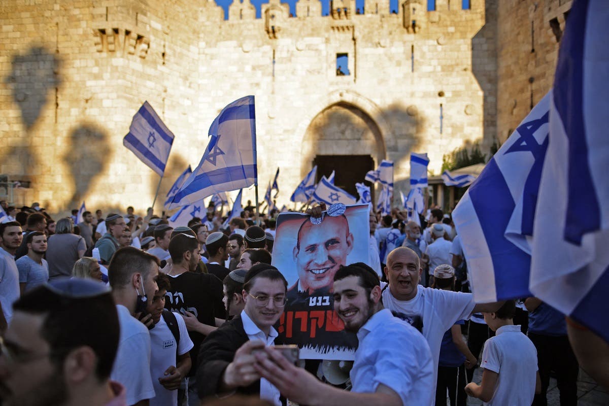 Israeli ultranationalists wave flags and a poster against PM Naftali Bennett during the March of the Flags near Jerusalem’s Old City, on June 15, 2021, celebrating the anniversary of Israel’s 1967 occupation of Jerusalem’s eastern sector. Hebrew on portrait reads: “Naftali is a liar.” (Ahmad Gharabli/AFP)