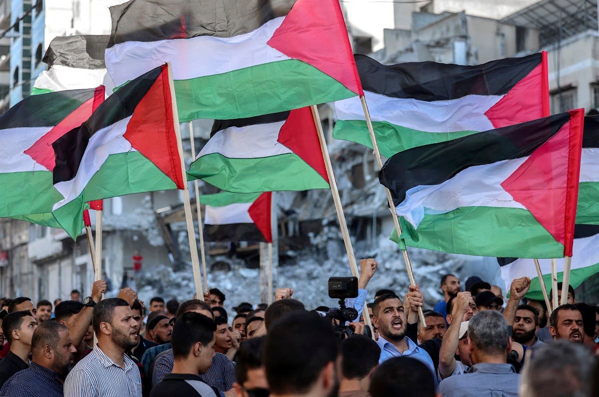 Palestinians lift national flags as they march past buildings destroyed by Israeli air strikes in Gaza City on June 15, 2021, during a protest over the Israeli ultranationalist March of the Flags in Jerusalem's Old City. (Mohammed Abed/AFP)