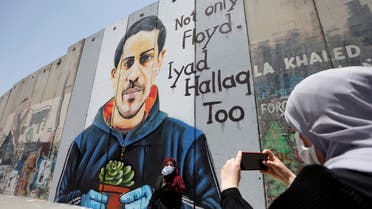 A Palestinian woman takes pictures of her friend posing in front of the Israeli barrier with a mural depicting Iyad al-Halaq, an unarmed and autistic Palestinian who was shot dead by Israeli police, in Bethlehem in the Israeli-occupied West Bank on June 18, 2020. (Reuters)