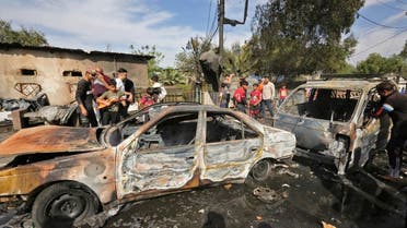 People gather around destroyed vehicles at the scene of an explosion in the Habibiya district of the Sadr City suburb of Iraq's capital Baghdad on April 15, 2021. (AFP)