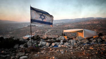 An Israeli flag flutters as smoke from fires lit in the nearby Palestinian village of Beita drifts past it, in Givat Eviatar, a new Israeli settler outpost in the Israeli-occupied West Bank June 23, 2021. Picture taken June 23, 2021. (Reuters)