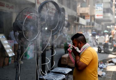 A man stands by fans spraying air mixed with water vapour deployed by donors to cool down pedestrians along a street in Iraq's capital Baghdad on June 30, 2021 amidst a severe heat wave. (AFP)