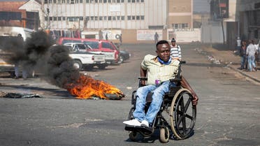 A protester in a wheelchair passes a burning tyre in Johannesburg, Sunday, July 11, 2021. (AP)